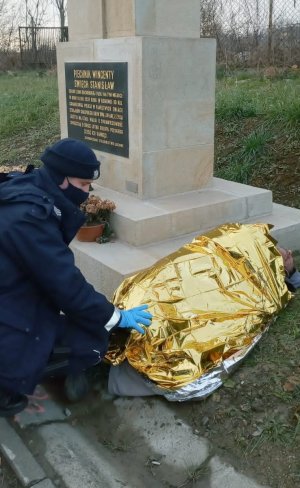 wychłodzony mężczyzna leżący przy pomniku, obok niego kuca policjant