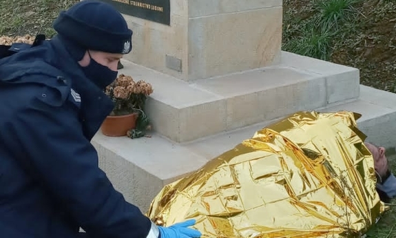 wychłodzony mężczyzna leżący przy pomniku, obok niego kuca policjant