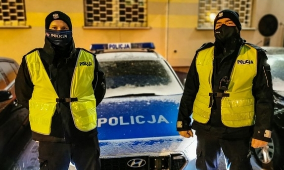 dwaj policjanci stoją przed radiowozem