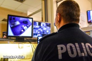 policjant siedzący przed monitorem obserwujący pomieszczenie z zatrzymanym mężczyzną