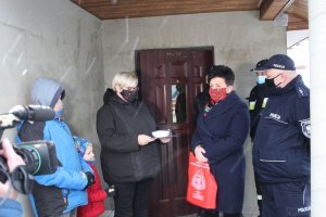 Zdjęcie z wręczenia czujników czadu we wsi Kruszewiec  na zdjęciu cztery osoby od lewej dziecko w kurtce niebieskiej, kobieta  otrzymująca  czujnik,  sołtys wsi Kruszewiec   oraz policjant