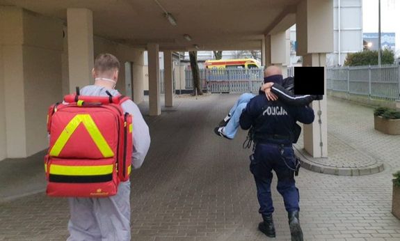 widać tyłem idącego ratownika medycznego i obok policjanta niosącego na rękach kobietę