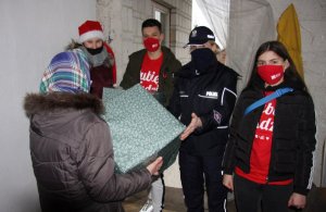 Umundurowana policjantka oraz osoby cywilne wręczające paczkę
