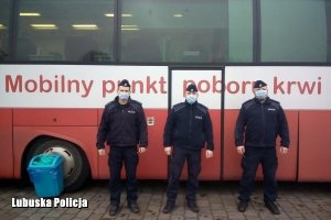 trzej policjanci stoją przed krwiobusem