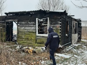 Policjant stojący przed spalonym domem