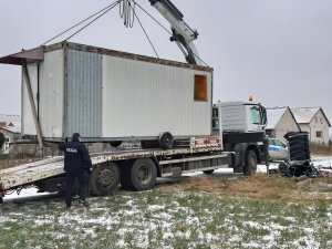 Kontener mieszkalny umiejscowiony na lawecie, obok policjant