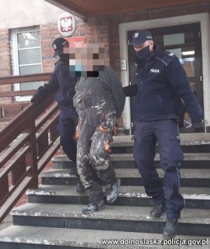 dwóch policjantów wyprowadza zatrzymanego mężczyznę z budynku komendy Policji