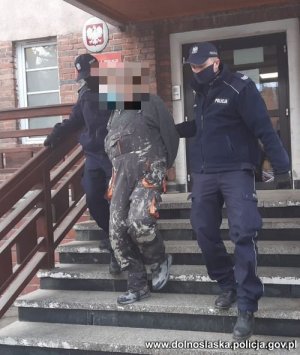dwóch policjantów wyprowadza zatrzymanego mężczyznę z budynku komendy Policji