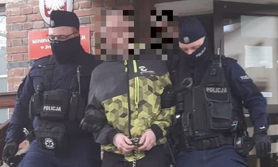 dwóch policjantów wyprowadza zatrzymanego mężczyznę z budynku komendy Policji