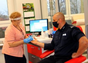 Policjant oddaje krew obok stoi pielęgniarka