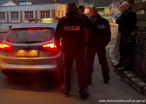 grupa policjantów z odnalezionym mężczyzną stoją obok radiowozu