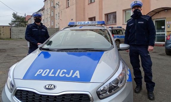 dwoje umundurowanych policjantów przy radiowozie