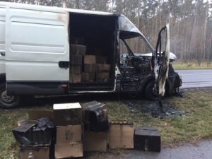 Auto dostawcze częściowo spalone. W przestrzeni załadunkowej widoczne przez otwarte drzwi kartony. Kilka kartonów stoi również na poboczu przez autem.&quot;&gt;