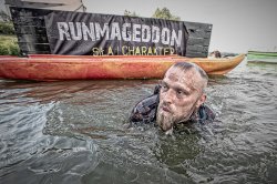 Mężczyzna płynie w wodzie zanurzony po szyję. W tle logotyop biegu Runmageddon