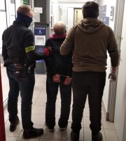 Zdjęcie kolorowe, na którym widać dwóch nieumundurowanych policjantów i mężczyznę znajdujących się w pomieszczeniu. Wszystkie osoby są odwrócone tyłem.