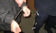 Policjant trzyma za rękę zatrzymanego, który ma założone kajdanki