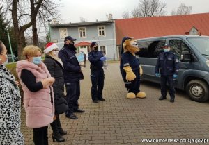 Funkcjonariusze oraz pracownica cywilna Policji przekazują upominki. W tle radiowóz policyjny i Komisarz Lew - maskotka dolnośląskiej Policji