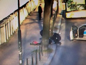 Policyjny radiowóz tarasuje drogę, ma otwarte drzwi. Policjanci udzielają pomocy osobie leżącej na chodniku.