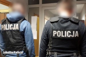 dwaj policjanci kryminalni w kamizelkach z napisem Policja stoją przed drzwiami