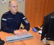 Umundurowany policjant siedzi przed komputerem przy biurku
