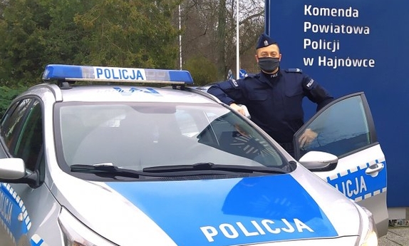 policjant stoi przy radiowozie policyjnym z otwartymi drzwiami