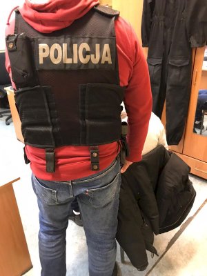 policjant stoi obok zatrzymanego mężczyzny siedzącego na krześle