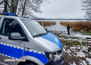 Dach policyjnego radiowozu, a w tle policjant sprawdzający czy na zamarzniętym jeziorze nie ma osób