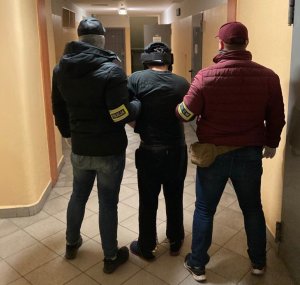 Zdjęcie kolorowe: dwóch policjantów wydziału kryminalnego katowickiej komendy na korytarzu  z zatrzymanym mężczyzna podejrzanym o usiłowanie zabójstwa