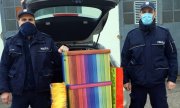 Policjanci stoją obok wielkich kolorowych kartonów z darami, a za nimi znajduje się otwarty bagażnik radiowozu