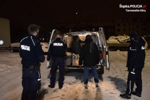 Na zdjęciu widać policjantów, pracownika socjalnego oraz bezdomnego mężczyznę, który wsiada do policyjnego radiowozu