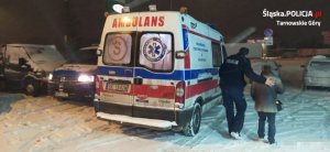 Na zdjęciu widać policjanta, który idzie z seniorką i pomaga jej dotrzeć do ambulansu