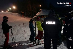 Na zdjęciu widoczni policjanci i narciarze. W tle widoczny stok