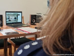 Na zdjęciu pokój, w którym znajduje się policjantka obserwująca obraz na laptopie podczas spotkania online.