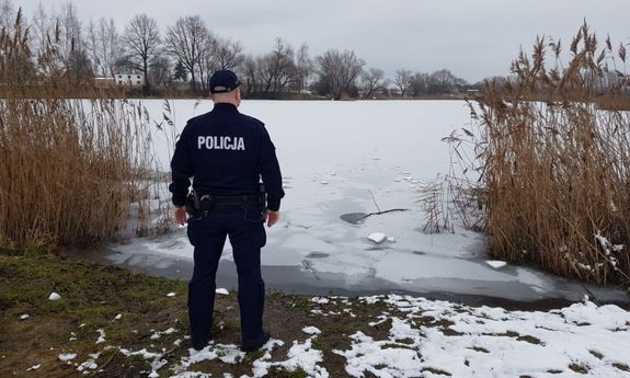 Umundurowany policjant stoi przed zamarzniętym zbiornikiem wodnym