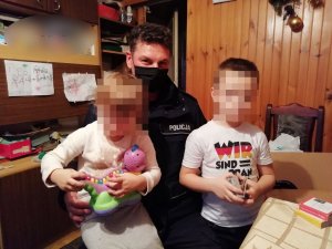 Policjant trzyma na kolanach dzieci z rodziny zastępczej, którą odwiedził