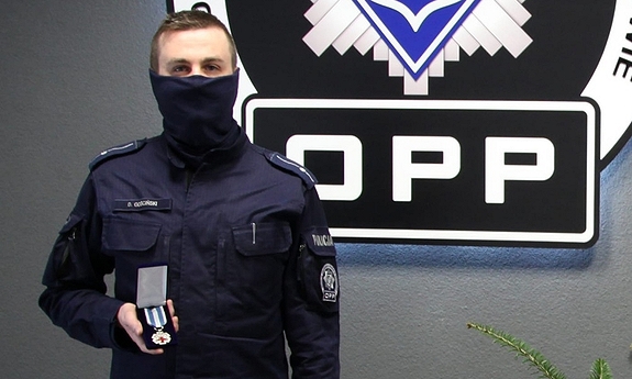 policjant pozuje z medalem w dłoni w tle na ścianie logo Oddziału Prewencji Policji