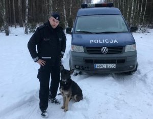 Policjant z Fioną w lesie. Zimowa sceneria. Za nimi stoi policyjny radiowóz