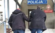policjant prowadzi zatrzymanego mężczyznę po schodach do komendy policji