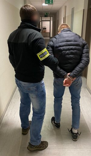 Policjant prowadzi zatrzymanego po korytarzu