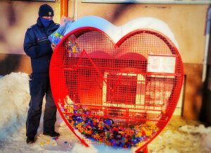 Policjant wrzuca plastikowe nakrętki do metalowego pojemnika w kształcie serca.