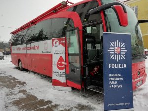 Na pierwszym zdjęciu znajduje się autobus z napisem Mobilny punkt poboru krwi. Po lewej stronie otwartych drzwi usytuowany jest baner koloru biało-czerwonego, na którym widnieje tekst: Nasza krew ratuje życie. Dołącz, zostań honorowym dawcą. HDK PCK Strażak przy OSP w Łęczycy. Po prawej stronie drzwi znajduje się baner koloru granatowego z logo Policji i napisem koloru białego Komenda Powiatowa Policji w Łęczycy