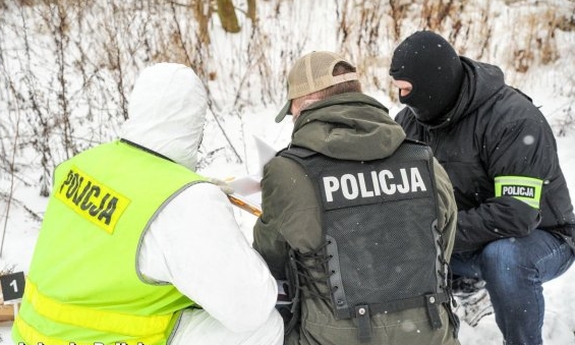 Policjanci śledczy i operacyjni w kamizelkach wraz z technikiem kryminalistyki przy oględzinach