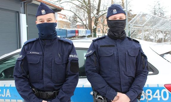 Dwaj policjanci stoją przed radiowozem