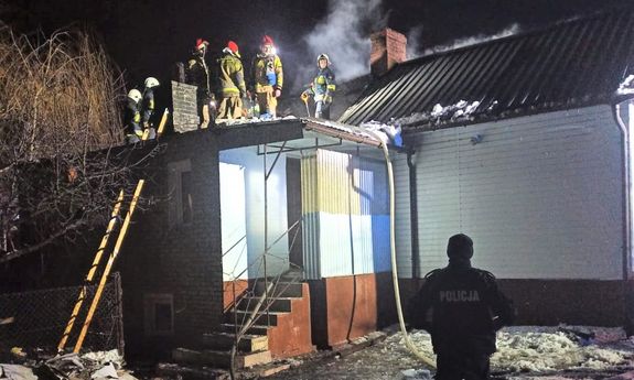 Stojący przed domem policjant, na dachu domu strażacy