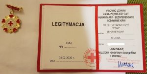 z lewej strony okrągła w kolorze złotym z napisem Honorowy dawca Krwi PCK obok otwarta legitymacja o nadaniu odznaki Honorowego Dawcy Krwi I Stopnia Zbigniew Mucha w dowód uznania za najpiękniejszy dar humanitarny – bezinteresowne oddawanie krwi