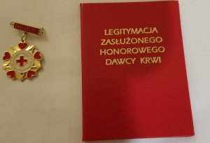 z lewej strony okrągła w kolorze złotym z napisem Honorowy Dawca Krwi PCK obok legitymacja  w kolorze czerwonym Zasłużony Honorowy Dawca Krwi