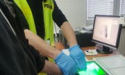 policjant wykonuje badanie daktyloskopijne z podejrzanym
