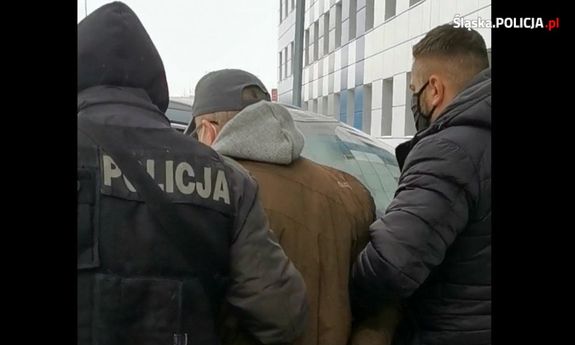 Policjanci prowadzą zatrzymanego mężczyznę, który na rękach ma założone kajdanki