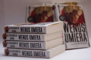 cztery książki Wenus umiera leżą jedna na drugiej w tle stojące książki