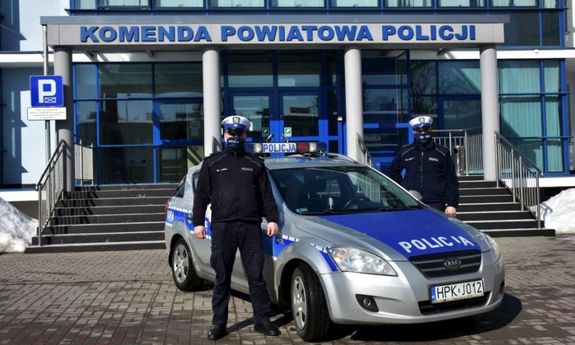 Policjanci wydziału ruchu drogowego stoją obok radiowozu. W tle budynek Komendy Powiatowej Policji w Jarosławiu